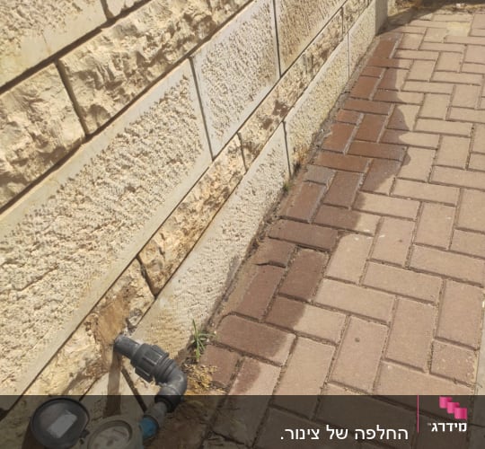 מד מים וצינור ליד קיר אבן